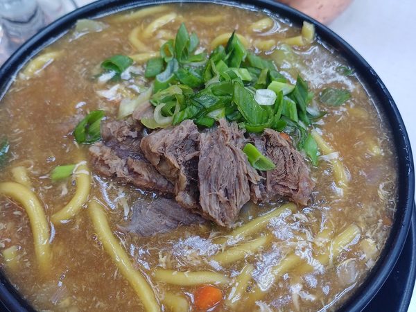Bowl of beef lomi, thick yellow noodles in a rich starchy broth topped with tender braised beef and sliced spring onions