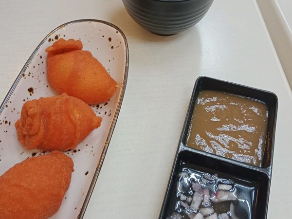 Three pieces of tokneneng, deep-fried battered egg, on a speckled oval plate with a two-part tray of sweet sauce and onion vinegar dip